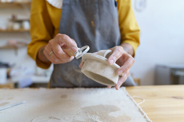 Working with raw clay: caucasian female ceramic studio owner shaping and modeling material for preparing jug in pottery workshop. Small handmade business, creative hobby and entrepreneurship concept