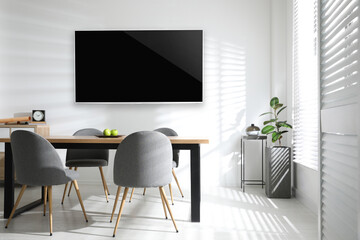 Modern wide screen TV on white wall in room with stylish furniture