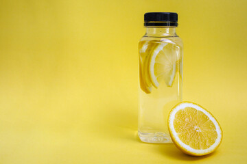 A bottle of water with slices of lemon on yellow background with copy space