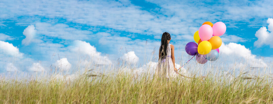 Banner Cheerful cute girl holding balloons running green meadow white cloud and blue sky with happiness. Panorama Hands holding vibrant air balloons happy times summer sunlight outdoor copy space