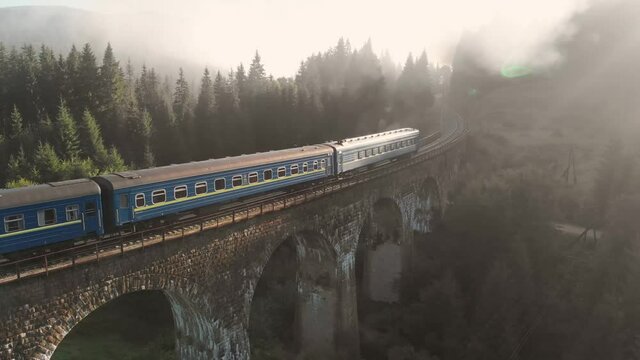 Aerial shot of a train crossing a beautiful stone bridge in early morning. 