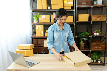 Woman packing box on table checking goods package delivery shipping to customer. Asian woman startup small business at home office desk. Entrepreneur asian woman packing product for delivery items