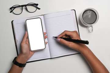 Above view woman holding smart phone and writing on notebook.