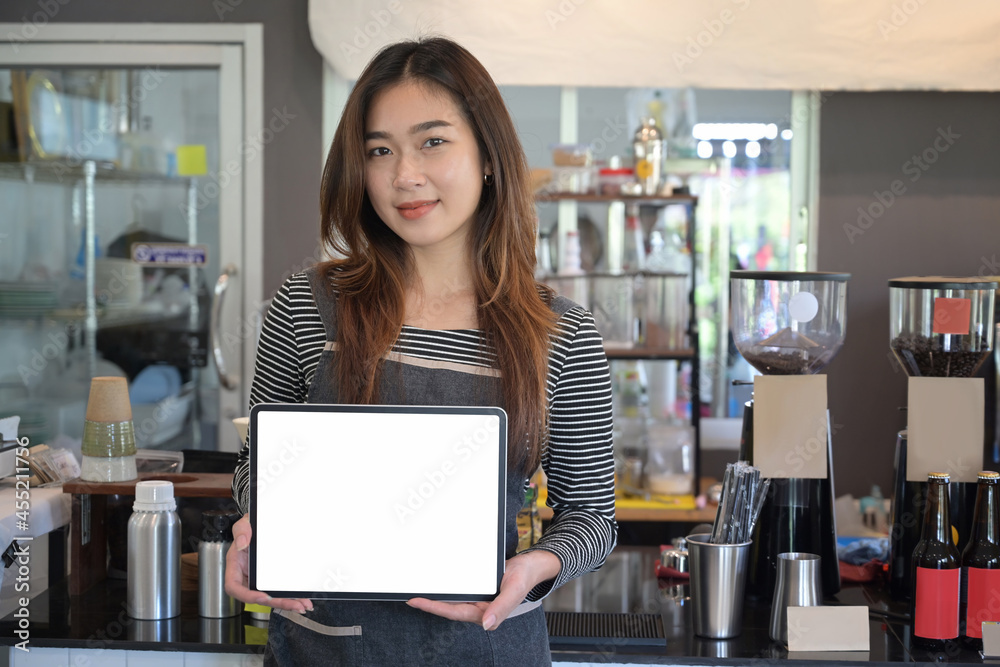 Wall mural young female entrepreneur in apron showing digital tablet while standing in modern cafe.