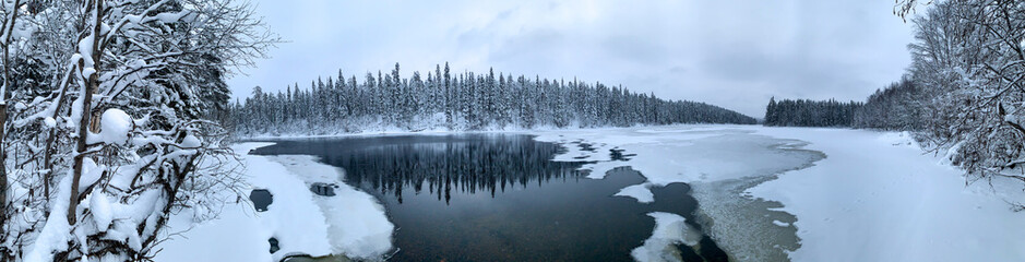 Panorama of an ice-covered river among a frozen taiga forest in a harsh winter