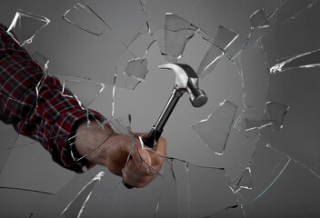 Man breaking window with hammer on dark grey background, closeup
