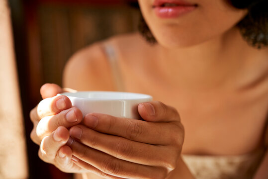 Close-up image of young woman holding cup of warm delicious herbal tea