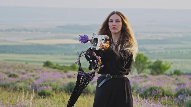 Funny Young Woman In Hippie Style With Goat Skull And Dreamcatcher In Hands On A Background Of Wild Lavender And Horizon. Beliefs.