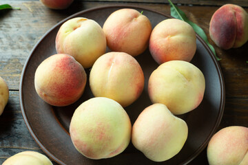 Ripe peaches in a clay plate on a wooden table with scattered leaves.