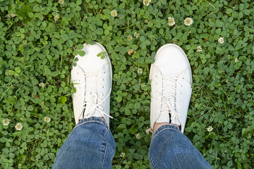 Legs in white leather sneakers on fresh green grass background. Nature walks in comfortable shoes.