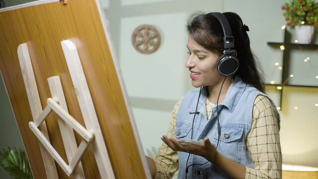 Young girl painting by enjoying music on headphones - Concept of hobby, enjoying art, leisure activities and taking break