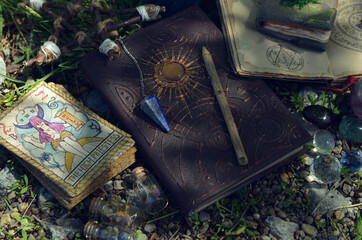 Magic book of spells, tarot cards and crystals on the grass in the garden.