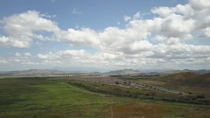 Slow drone shot from right to left with clouds white and puffy.
green grass in an open field.
no color grading done.