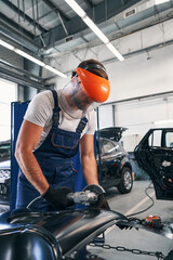 Auto mechanic in face shield grinding a car detail