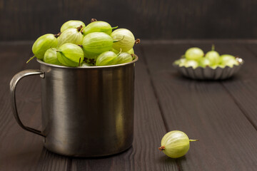 Green gooseberries in metal mug. Berry on table