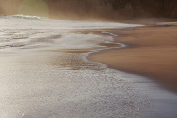 Sandy ocean coastline at sunset with foamy wave, sun glare and light. Beautiful natural sea...
