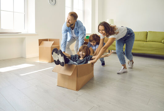 Happy family having fun in new home. Joyful excited first-time buyers with children playing with cardboard boxes in living room interior. Real estate, residential mortgage, buying dream house concept