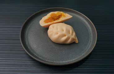 steamed fresh curry potato vegan bun orange baozi in leaf shape on dark grey wood background dim...