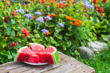 Slices of fresh red watermelon on a plate on a wooden surface in the garden against a background of...