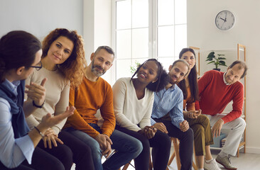 Team of happy diverse people talking sitting on row of chairs in office meeting. Group of colleagues, community members and friends communicating, sharing ideas and listening to each other's opinions