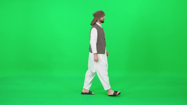 Man of Arab appearance in traditional clothes walking down the street against the green background, chromakey template.