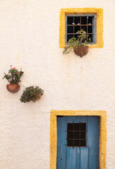 Fototapeta na wymiar Windows with yellow frame, blue door and traditional Spanish flowerpots on white wall in Nijar, Andalusia, Spain