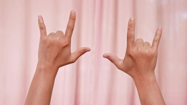 Hands making I Love You symbol on pink background. female hands Saying " I Love You " in Sign Language. Valentine's Day.