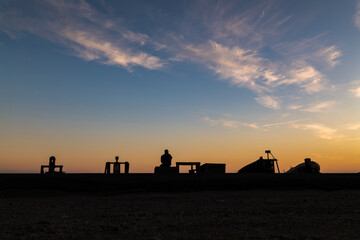 Silhouette of adult man looking at view on beach with fishing boat and winch during sunset