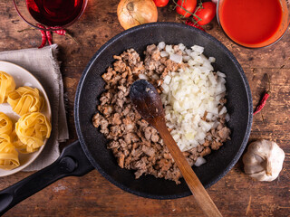 Cooking American-Italian pasta with sausage stew - frying pan with cooking stew and ingredients for the dish next to the table, fettuccine, wine, tomato sauce, onions, tomatoes and garlic with chili