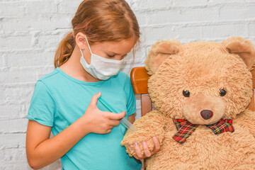 the child girl with a syringe makes an injection vaccination toy bear photo without processing
