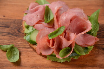 Open ham Sandwich with cucumbers, basil, and a crusty slice of rye bread and salami