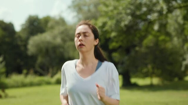 A young woman is jogging in the park, stops because of shortness of breath and continues running. Slow motion. The concept of wellness.