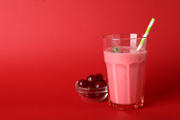 Glass of cherry smoothie and ingredients on red background