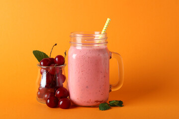 Glass jar of cherry smoothie and ingredients on orange background