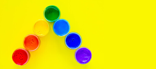 The paint cans stand at an angle, the colors are displayed in the order of the rainbow on a yellow background with space for the text. top view, flat lay, copy space, isolate