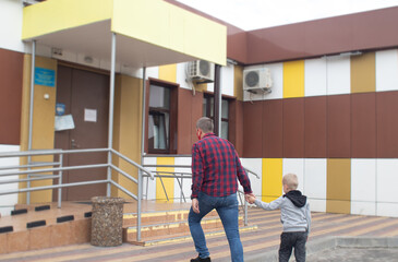Dad takes his son to the doctor. Against the backdrop of a standard hospital building, father and son prepare for an examination. Concept of a single parent preparing a child for school or kindergarte