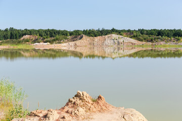 Lake on-site of abandoned ilmenite quarry against forest, sky