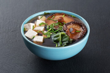 Miso soup with shiitake mushrooms, tofu cheese, fresh onions and wakame seaweed on a slate board background.