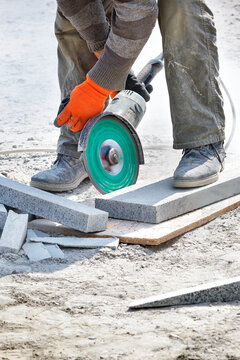 A builder uses a grinder and diamond cutting disc to cut granite blocks. Vertical image.