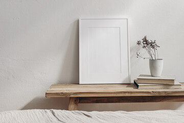 Vertical white picture frame mockup. Vintage wooden bench, table. Cup with dry grass on pile of books. White wall background. Scandinavian interior, neutral color palette. Selective focus. Art display - Powered by Adobe