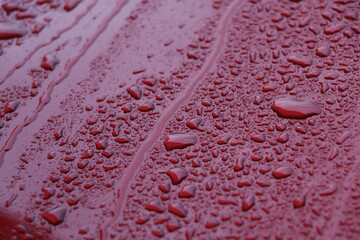 Raindrops on red car surface with beautiful bokeh effect from sunlight. Rain background 