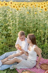 Fototapeta premium Young couple having picnic on sunflower field at sunset