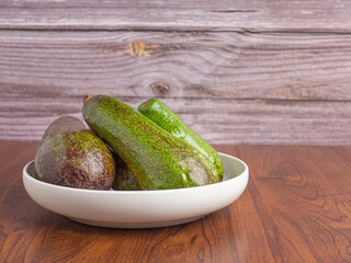 Avocados are served on a white plate with a wooden background. Side view. Space for text. Healthy fruits concept