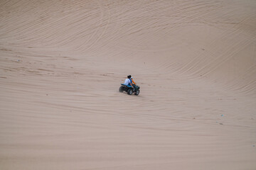 Fototapeta na wymiar Picturesque view of driving ATV in desert and tire tracks on sand on sunny day during summer vacation. Two people driving ATV in white sand dunes