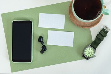 Cropped shot of male style, smart phone on green modern office desk with business card, tea cup, watch.