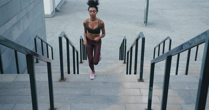 Sportive black woman runs up stairs with railings on street