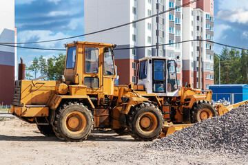 Fototapeta na wymiar Powerful wheel loader for transporting bulky goods at the construction site of a modern residential area. Construction equipment for lifting and moving loads.