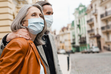 White senior couple in face masks hugging while walking on street