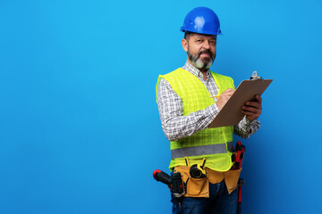 Male builder or handyman in uniform holding clipboard against blue background