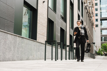 White senior man with beard using mobile phone while walking on street